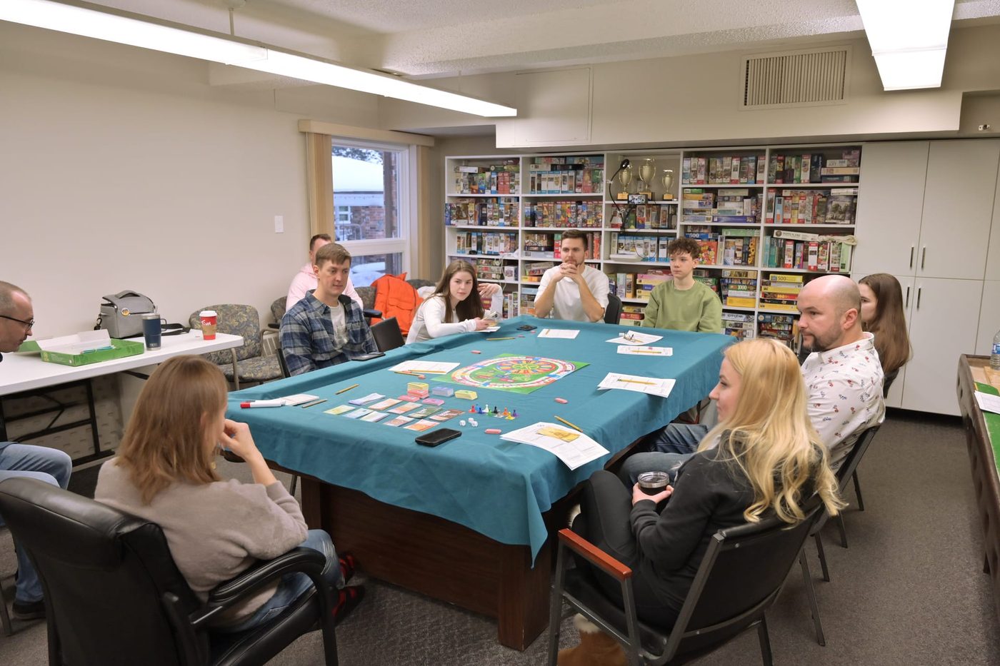 Adults around a Life Capital board mid-session, with ledger sheets and card decks on the table.
